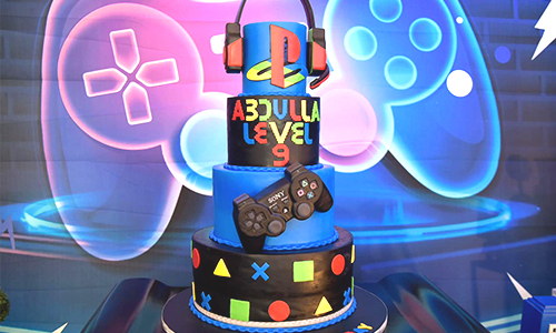 PlayStation-themed birthday cake with headset, controller and neon gaming backdrop.